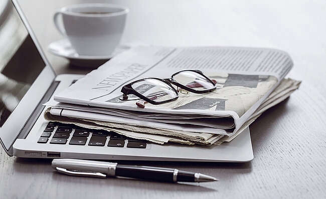 Ein Büro-Arbeitsplatz mit einem Laptop, einer Zeitschrift, einer Brille und einer Kaffeetasse
