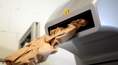 Aus einer Papierpolstermaschine kommt ein etwas flacherer zusammengestauchter brauner Papierpolsterstrang.