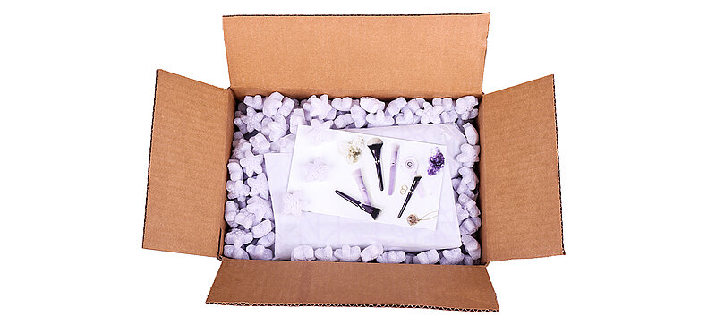 Ein Karton mit Kosmetikprodukten und lilafarbenen sternförmigen Verpackungschips