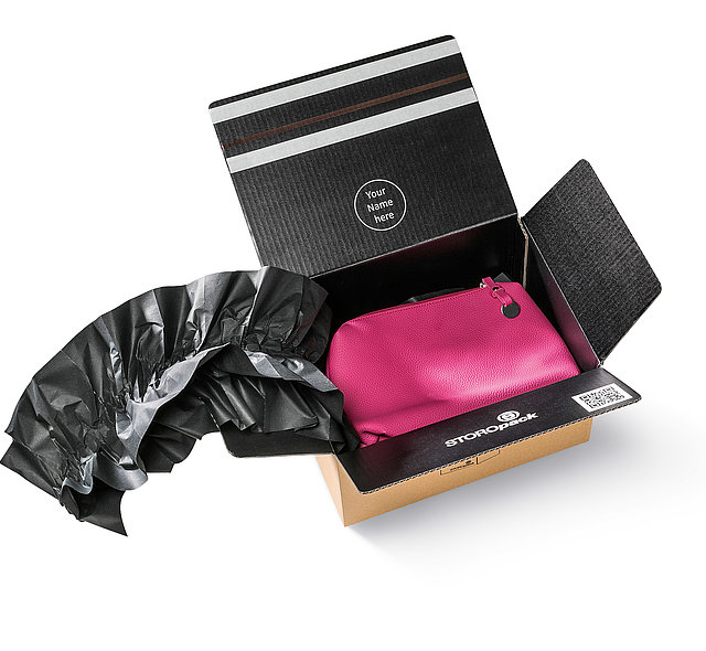 Ein Karton mit einer pinkfarbenen Tasche und schwarzen Papierpolstern