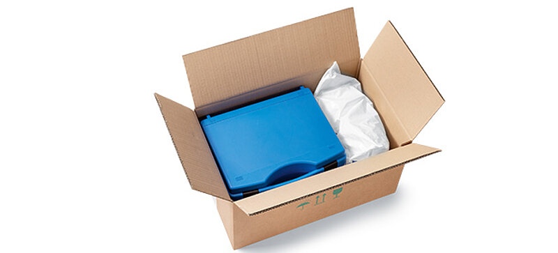 Ein Karton mit einem blauen Koffer und Kunststoffbeuteln mit Verpackungschips
